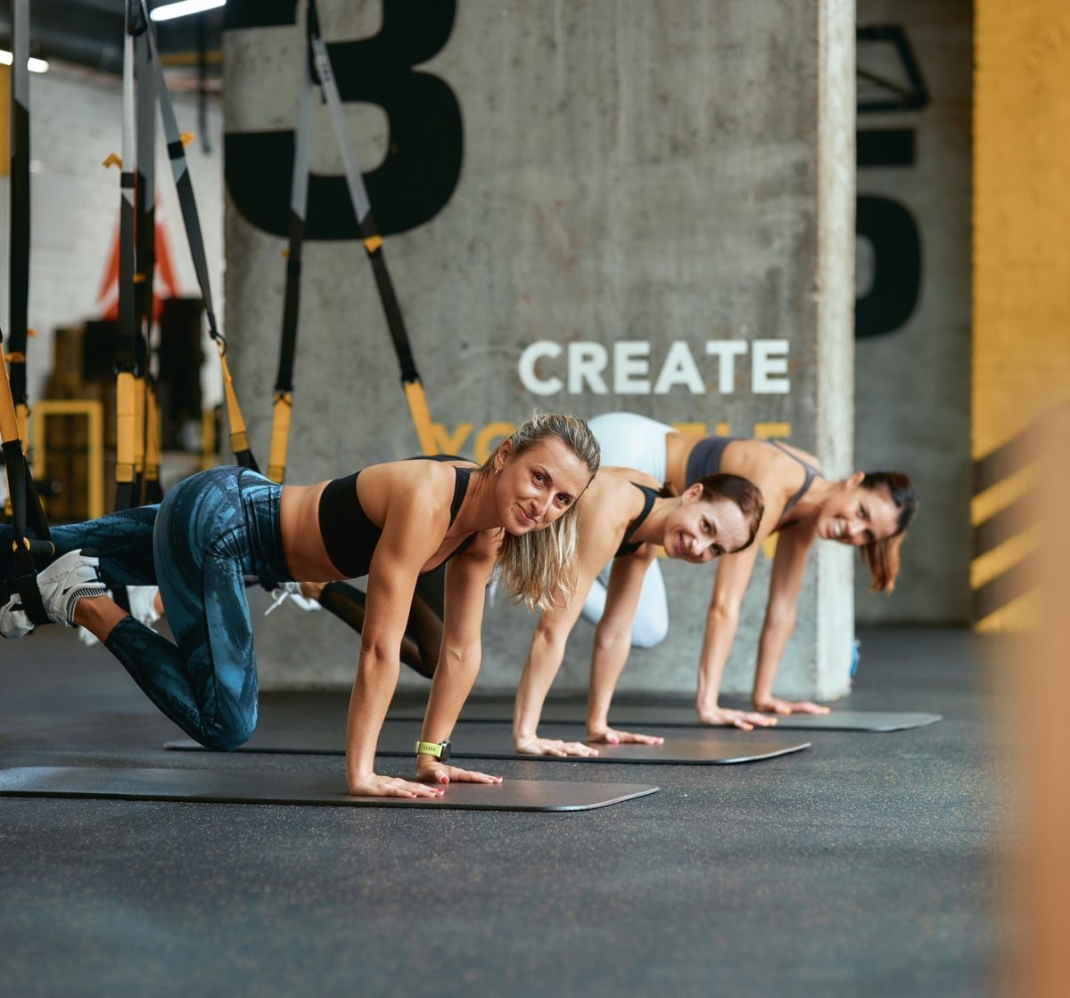 three-young-positive-girls-smiling-at-camera-while-exercising-with-trx-fitness-straps-at-gym.jpg